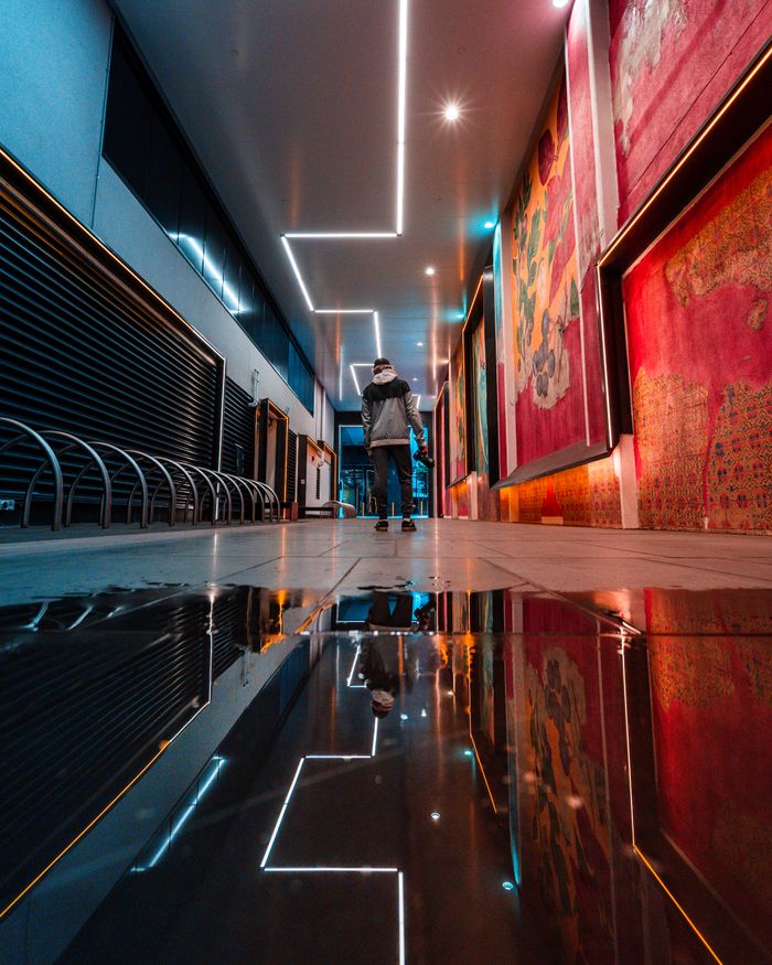 services-01 Person walking through a reflective, illuminated urban hallway with vibrant wall art.