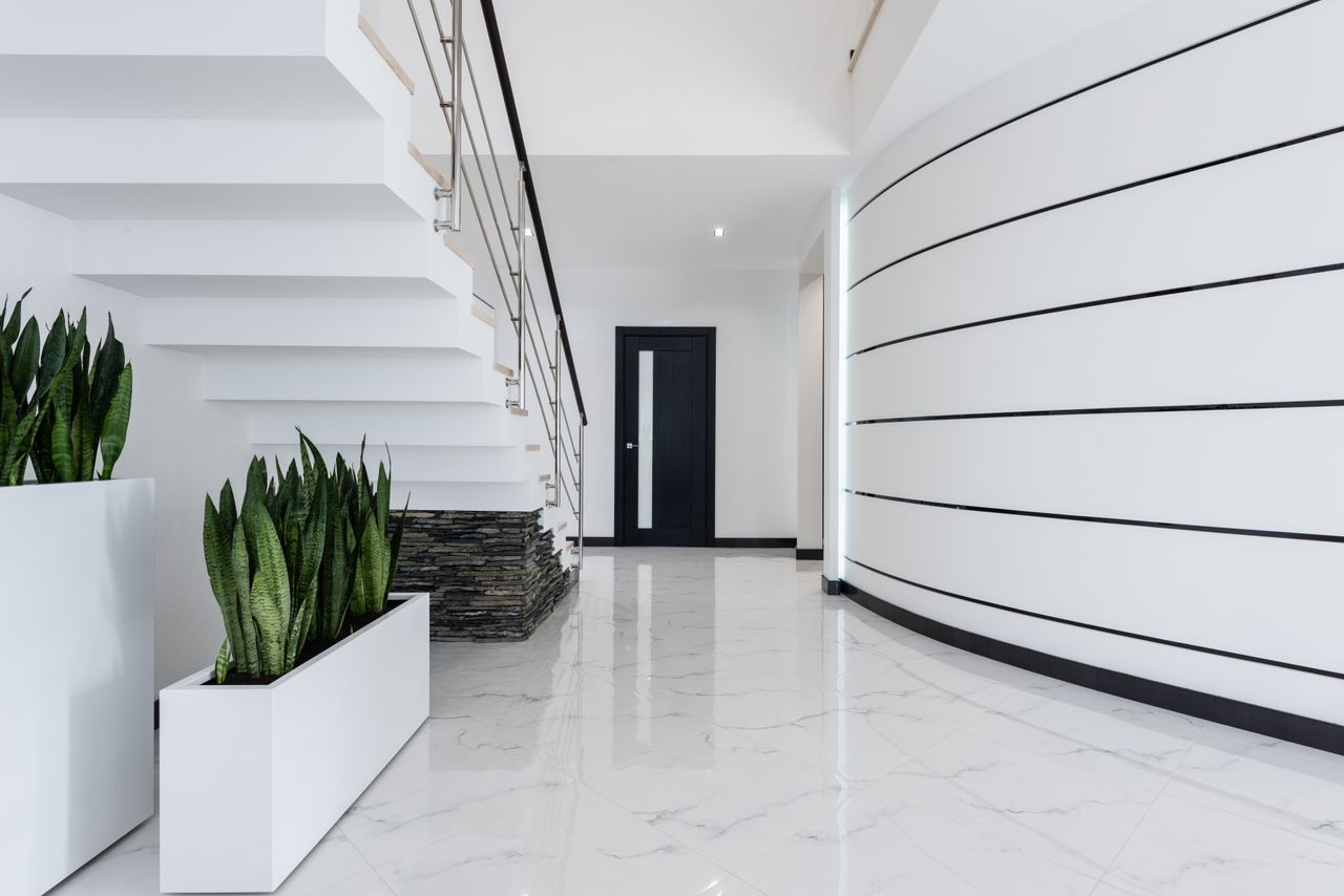 Interior of spacious hallway of modern villa with staircase and shiny marble effect floor decorated with fresh green potted plants